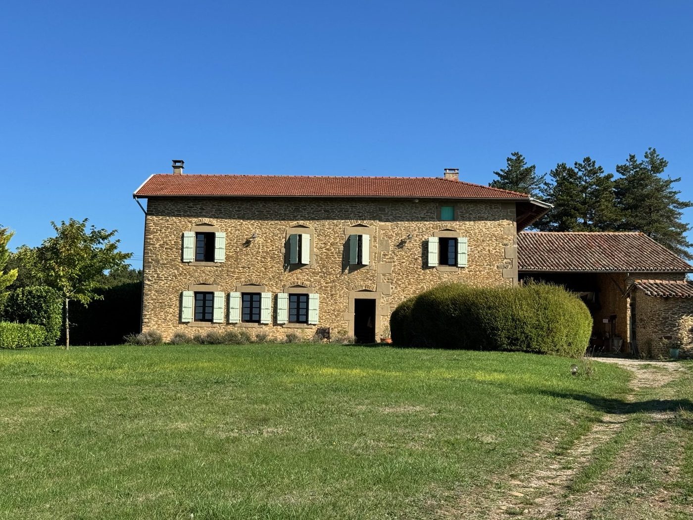 Façade de la maison en pierres dorées sous un ciel bleu, pelouse au premier plan