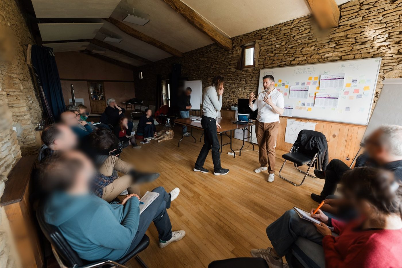 Frédéric Angelot anime un groupe assis au sol et sur des chaises dans la grande salle, devant un tableau de post-it